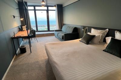 Chambre moderne avec lit double, bureau équipé, grande fenêtre avec vue sur les toits et éclairage suspendu.