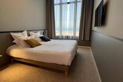 Chambre moderne avec lit double, bureau équipé, grande fenêtre avec vue sur les toits et éclairage suspendu.