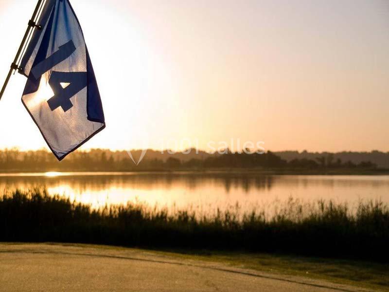 Drapeau bleu marqué ’14’ flottant près d'un lac au coucher de soleil, avec des arbres en arrière-plan.
