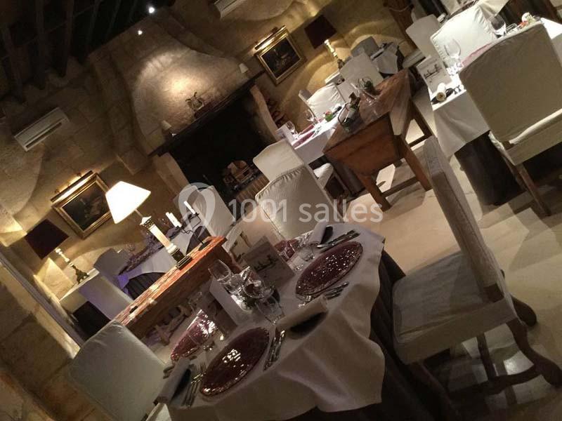 Salle de restaurant élégante avec tables dressées, nappes blanches et éclairage tamisé dans un cadre rustique.