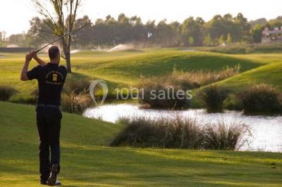Chambre lumineuse avec lit double, deux tables de chevet, lampes murales, fauteuil et rideaux à motifs floraux.