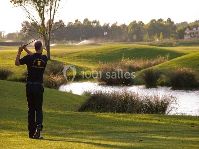 Un golfeur effectue un swing sur un terrain verdoyant près d'un plan d'eau, entouré de végétation et d'arbres.