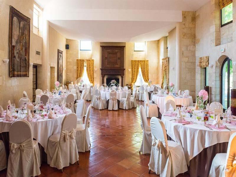 Salle de réception lumineuse avec tables rondes décorées, nappes blanches et chaises ornées de nœuds beiges.