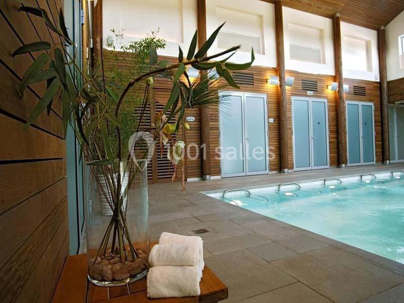 Piscine intérieure entourée de murs en bois, avec des plantes décoratives et des serviettes posées sur une table.