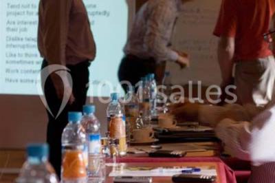 Chambre lumineuse avec lit double, deux tables de chevet, lampes murales, fauteuil et rideaux à motifs floraux.