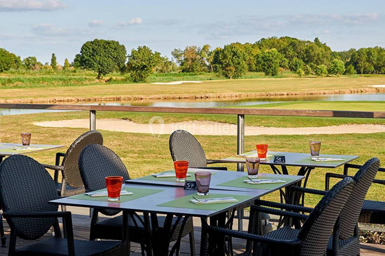 Terrasse d'un restaurant avec des tables dressées, offrant une vue sur un terrain de golf et un plan d'eau.
