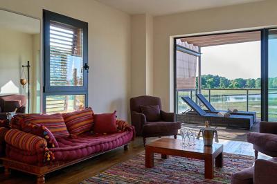 Chambre lumineuse avec lit double, deux tables de chevet, lampes murales, fauteuil et rideaux à motifs floraux.