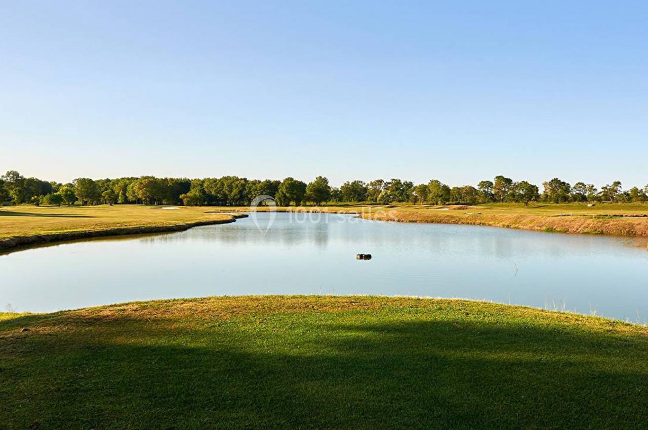 Plan d'eau entouré de pelouses et d'arbres sous un ciel dégagé en pleine journée.