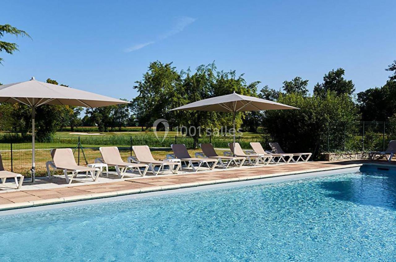 Piscine extérieure avec transats et parasols, entourée de verdure sous un ciel dégagé.