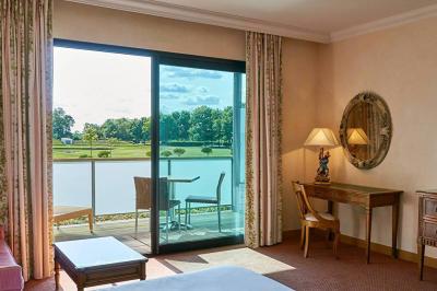 Chambre lumineuse avec lit double, deux tables de chevet, lampes murales, fauteuil et rideaux à motifs floraux.