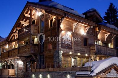 Chalet en bois éclairé de nuit avec balcons, toit enneigé et enseigne ’La Tapiaz’.