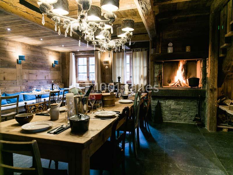 Salle à manger chaleureuse avec table dressée, cheminée allumée et décoration en bois rustique.