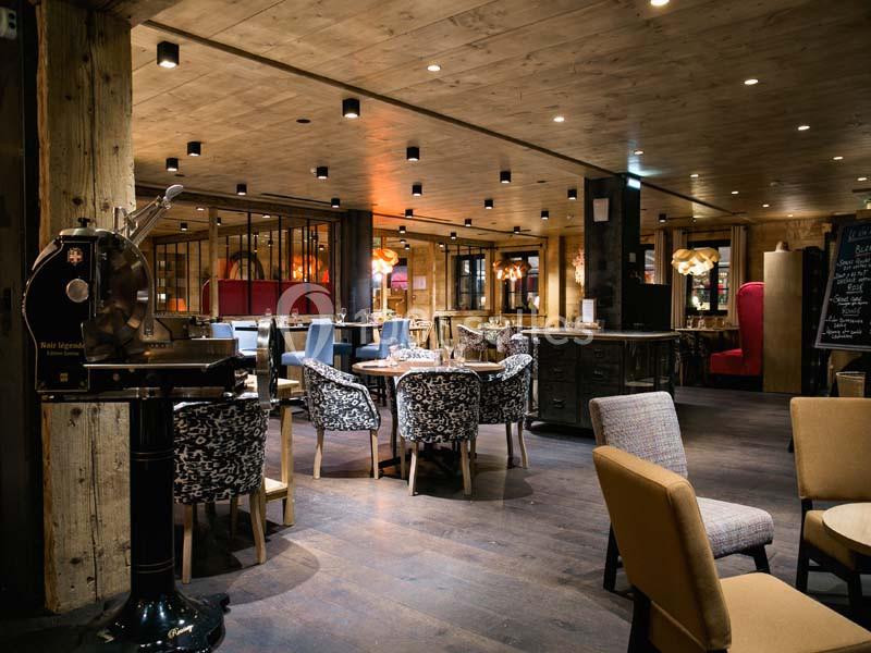 Salle de restaurant chaleureuse avec mobilier en bois, chaises variées et éclairage tamisé.