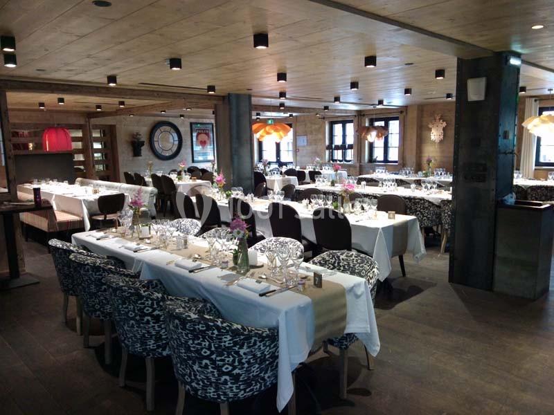 Salle de restaurant élégante avec tables dressées, chaises rembourrées et éclairage chaleureux sous un plafond en bois.