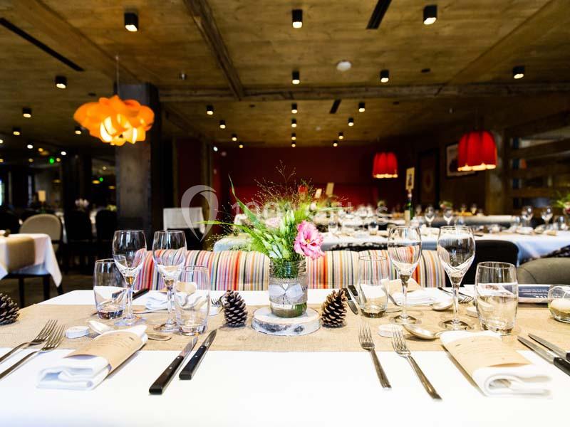 Salle de restaurant décorée avec des tables dressées, ornées de fleurs, de pommes de pin et de nappes élégantes.