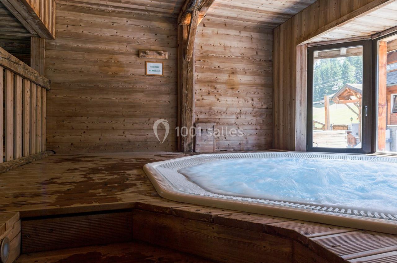 Jacuzzi bouillonnant dans un espace intérieur en bois avec vue sur un paysage extérieur ensoleillé.