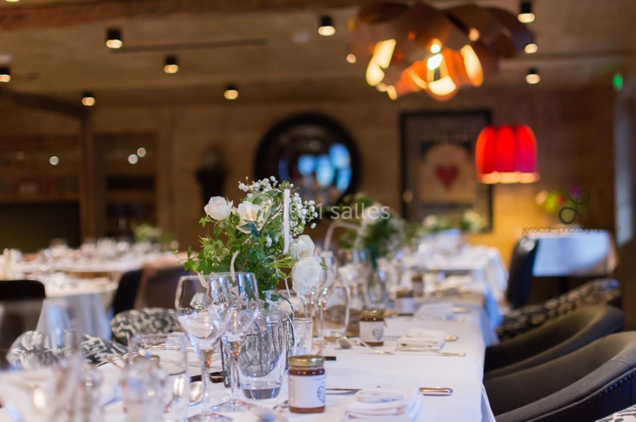 Salle de restaurant élégante avec tables dressées, décorées de fleurs blanches et éclairées par une lumière chaleureuse.