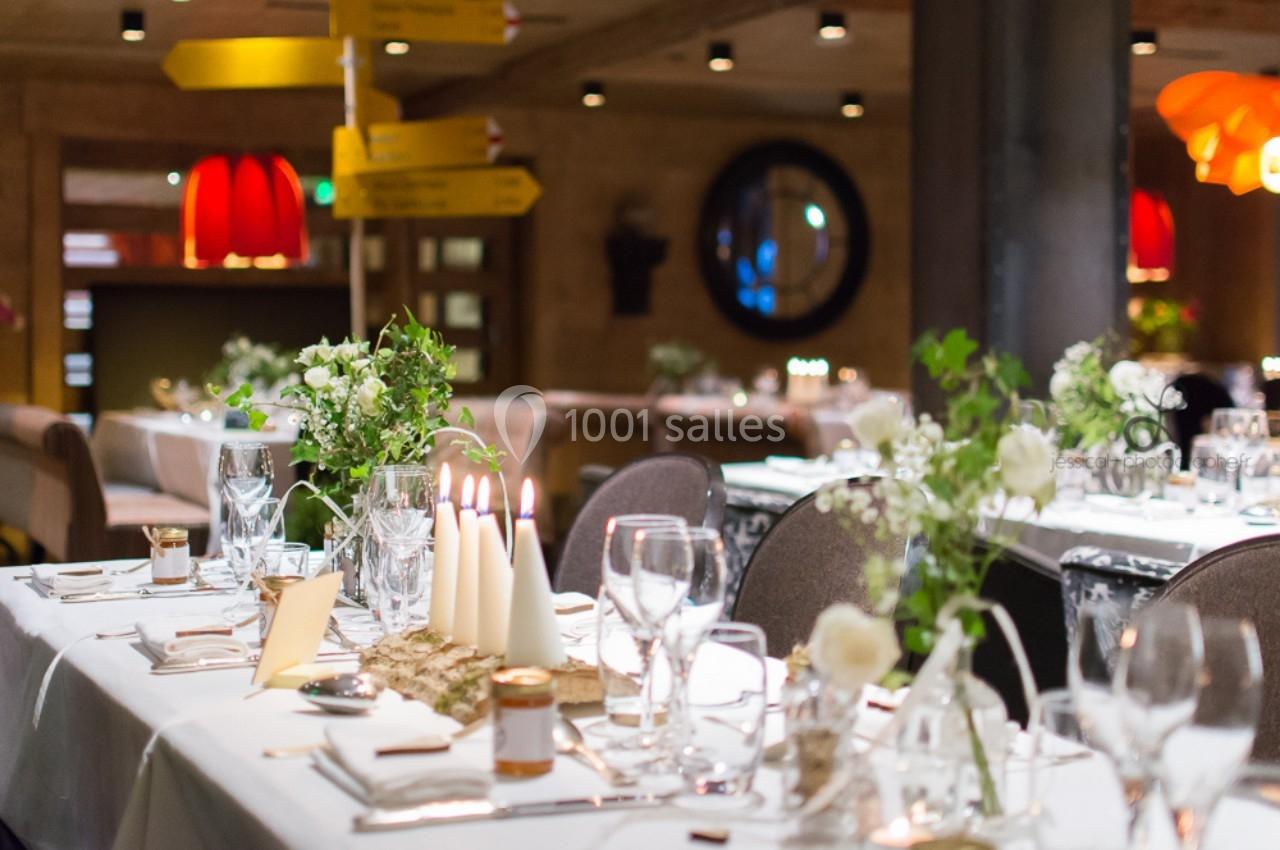 Tables élégamment dressées avec bougies, fleurs blanches et vaisselle raffinée dans un restaurant chaleureux.