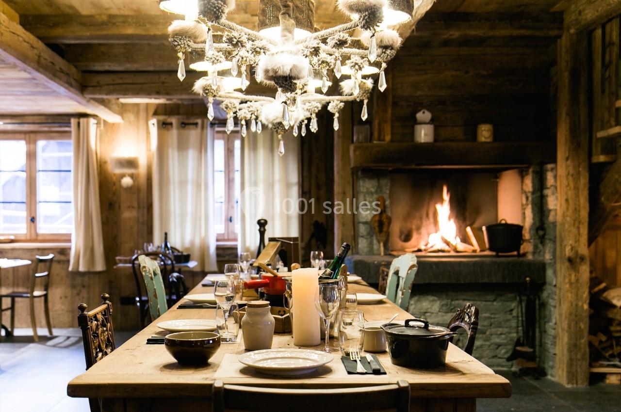 Salle à manger rustique avec table dressée, cheminée allumée et lumière tamisée dans un décor en bois chaleureux.