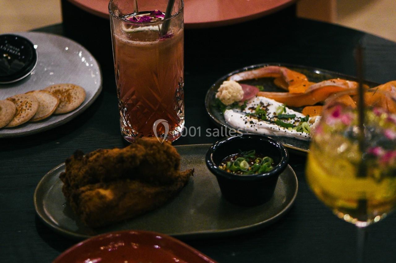 Assortiment de plats et cocktails sur des tables, incluant viande, poisson fumé, pain et accompagnements.