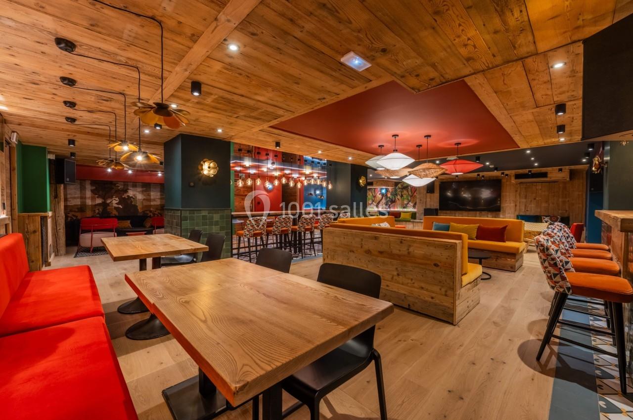 Salle moderne avec tables en bois, banquettes colorées, éclairage suspendu et décoration chaleureuse en bois.