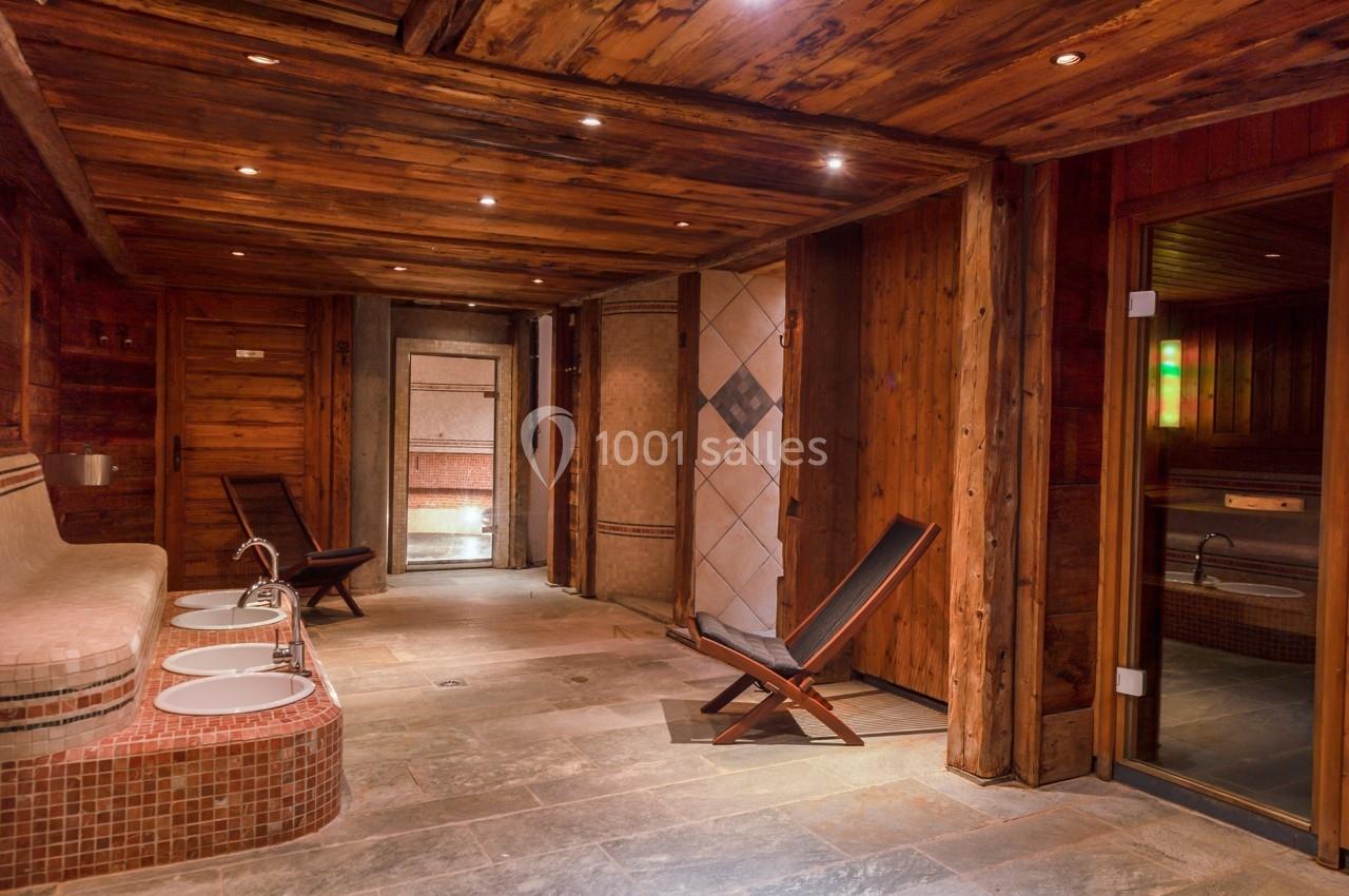 Espace spa avec murs en bois, chaises longues, douches carrelées et éclairage tamisé.