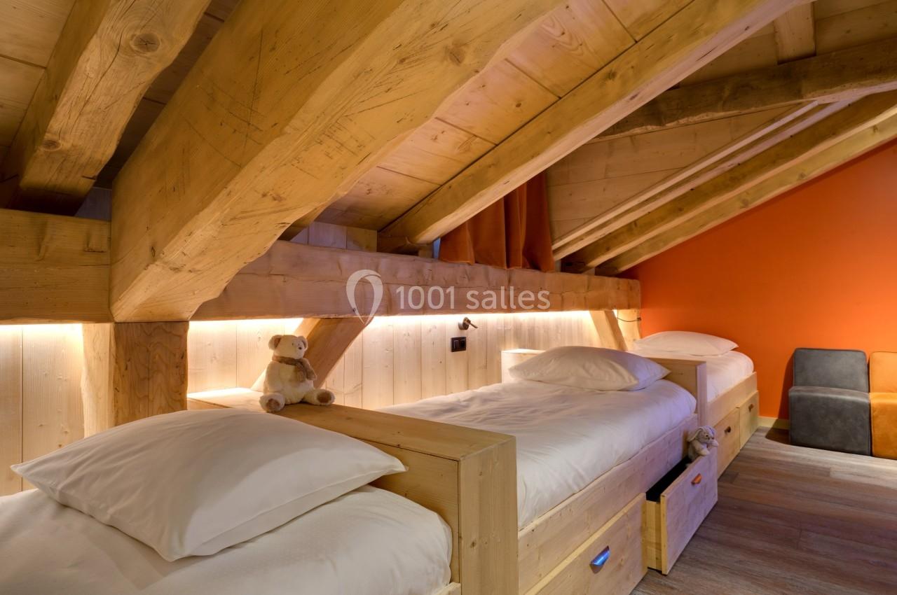 Chambre mansardée avec deux lits simples en bois, éclairage doux et murs en bois et orange.