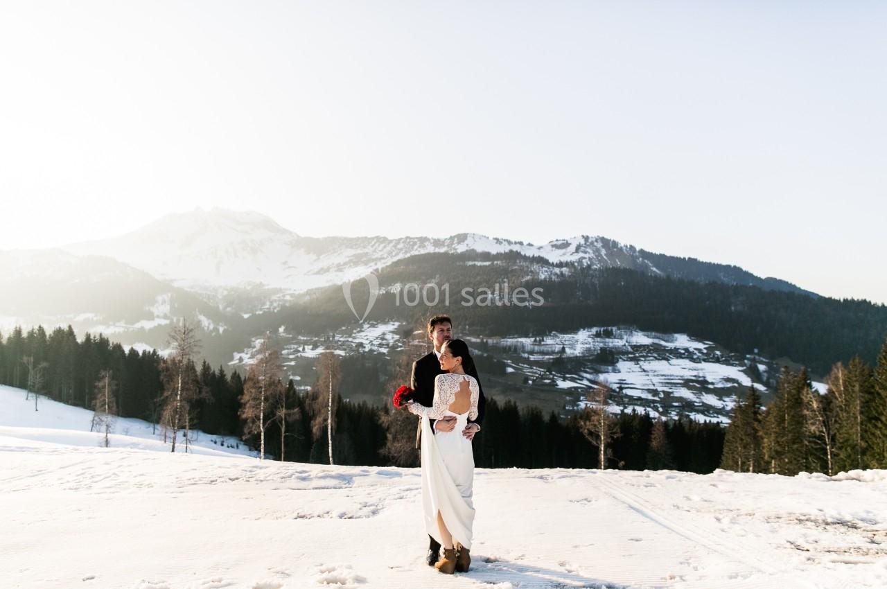 Un couple en tenue de mariage pose dans un paysage enneigé avec des montagnes en arrière-plan.