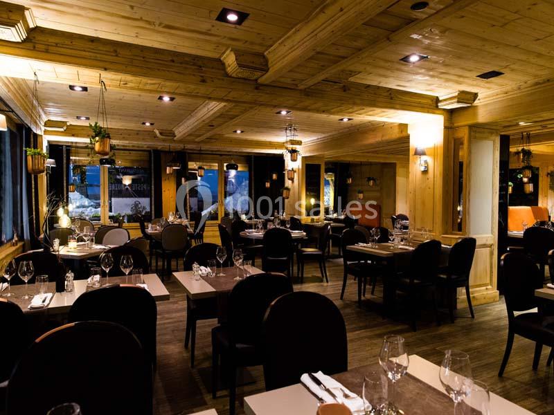 Salle de restaurant chaleureuse avec mobilier en bois, tables dressées et éclairage tamisé.