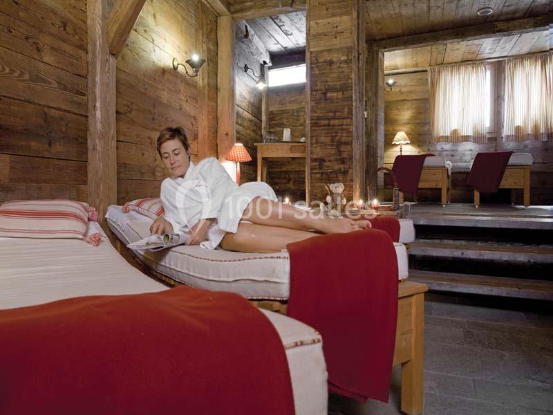 Femme en peignoir lisant sur un lit dans une pièce en bois avec lumière tamisée et bougies allumées.