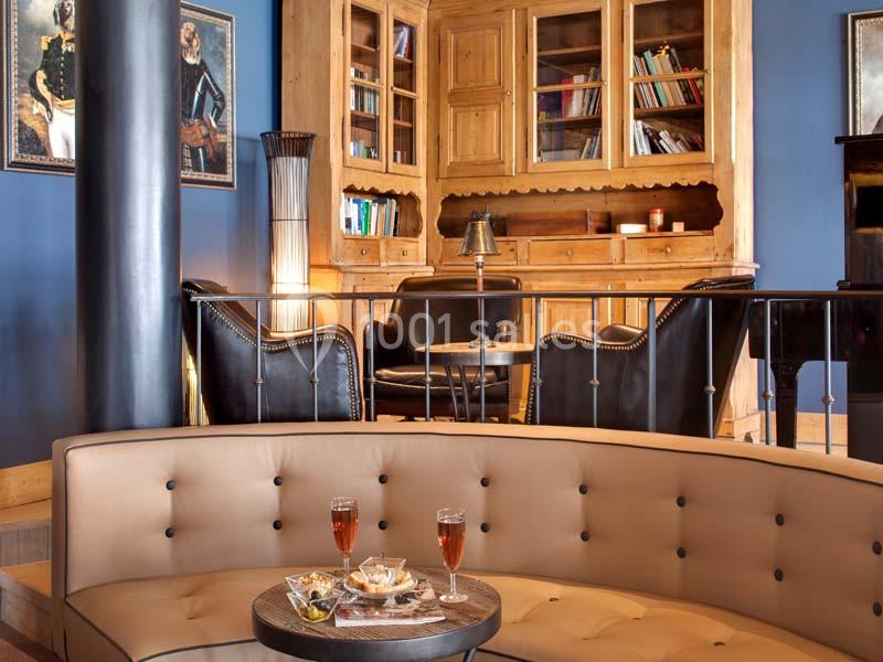 Salon élégant avec canapé beige, fauteuils en cuir noir, bibliothèque en bois et table basse avec boissons et snacks.