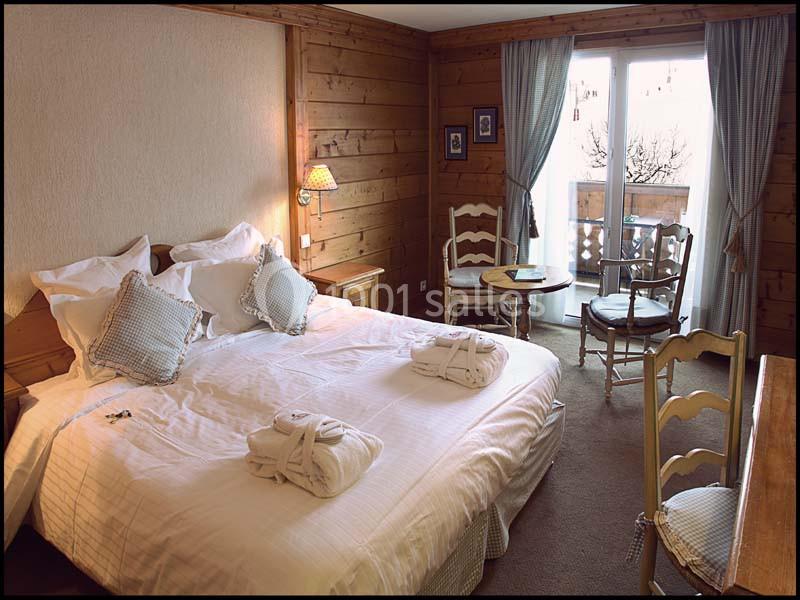 Chambre confortable avec lit double, mobilier en bois, lumière naturelle et accès à un balcon avec vue extérieure.