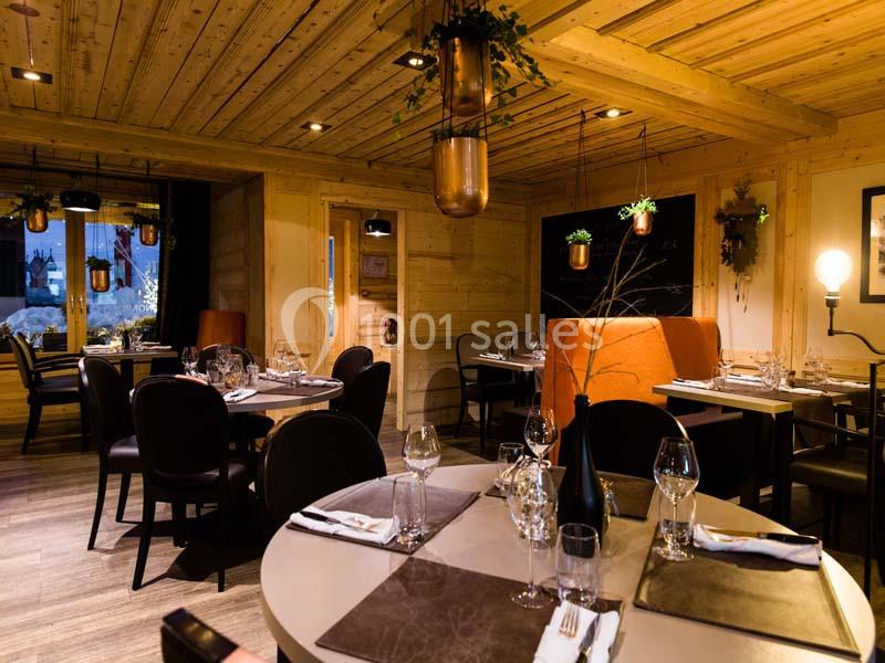 Salle de restaurant chaleureuse avec décoration en bois, tables dressées et lumières tamisées.