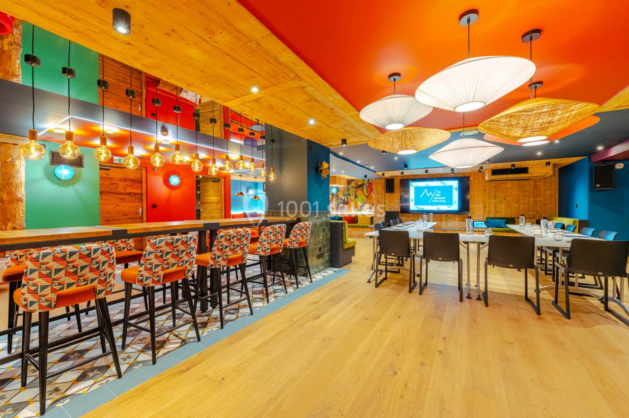 Salle colorée avec bar, chaises hautes, tables dressées, éclairage design et décoration moderne en bois et motifs variés.