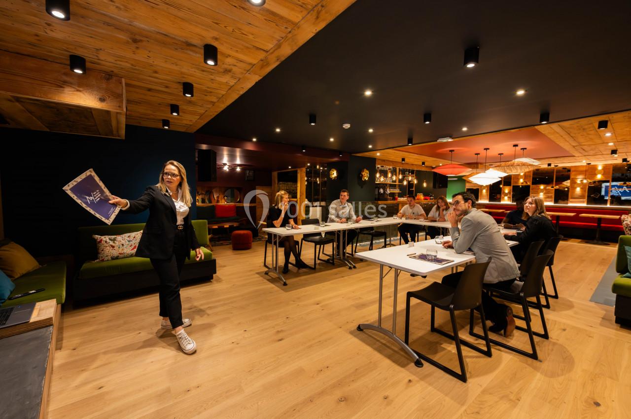 Une femme présente un document à un groupe de personnes assises dans une salle moderne avec un éclairage chaleureux.