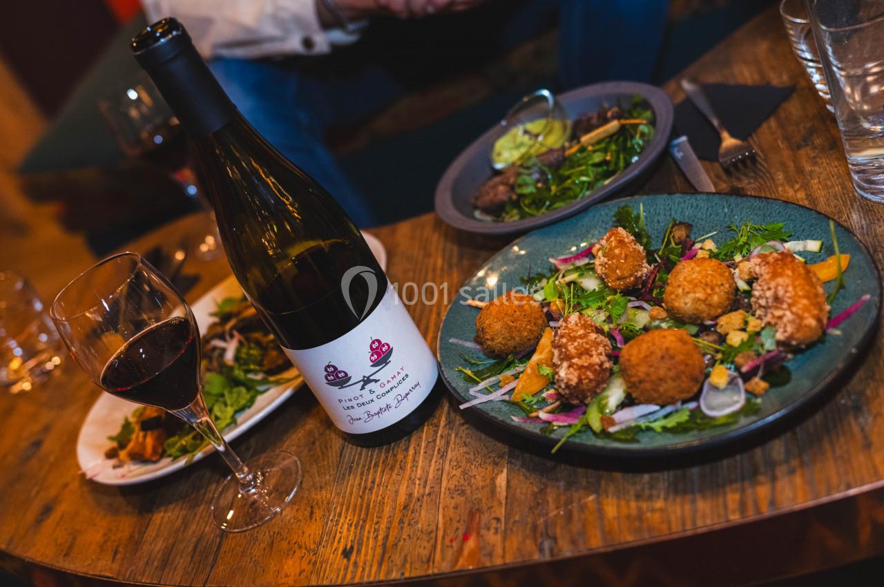 Assiette de croquettes avec salade, verre de vin rouge et bouteille posés sur une table en bois.