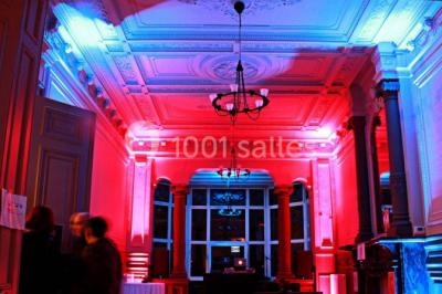 Grande maison en briques rouges avec deux tours, entourée de pelouse et de voitures garées devant.