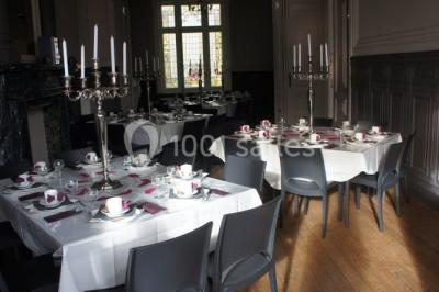 Grande maison en briques rouges avec deux tours, entourée de pelouse et de voitures garées devant.