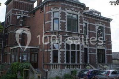 Grande maison en briques rouges avec deux tours, entourée de pelouse et de voitures garées devant.
