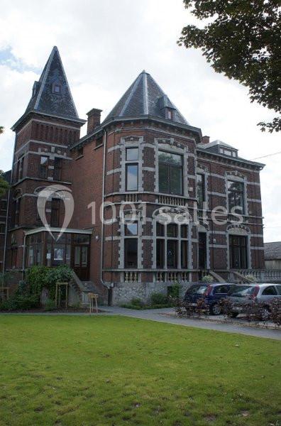 Grande maison en briques rouges avec deux tours, entourée de pelouse et de voitures garées devant.