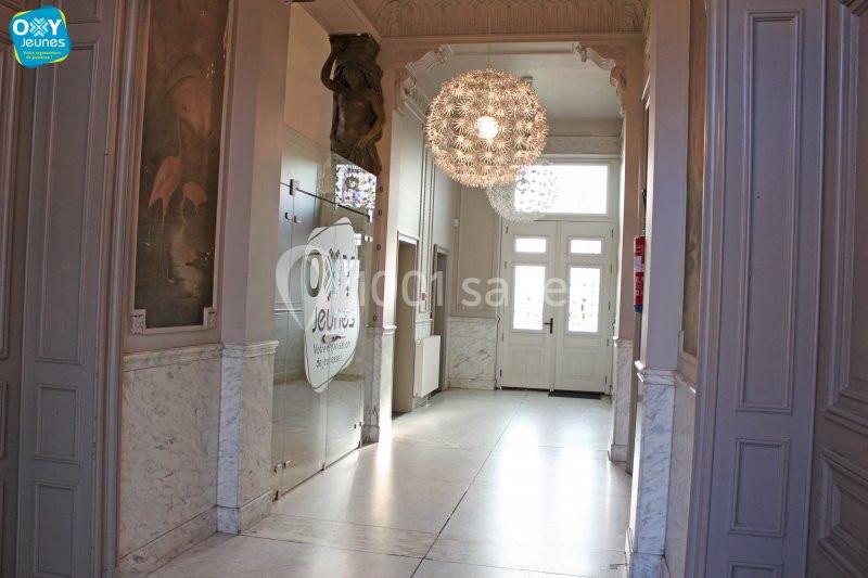 Entrée lumineuse avec portes vitrées, lustre moderne et murs ornés de moulures et de panneaux décoratifs.