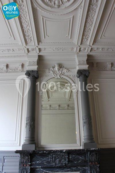 Miroir encadré de colonnes grises et orné de sculptures, placé au-dessus d'une cheminée en marbre noir dans une pièce…