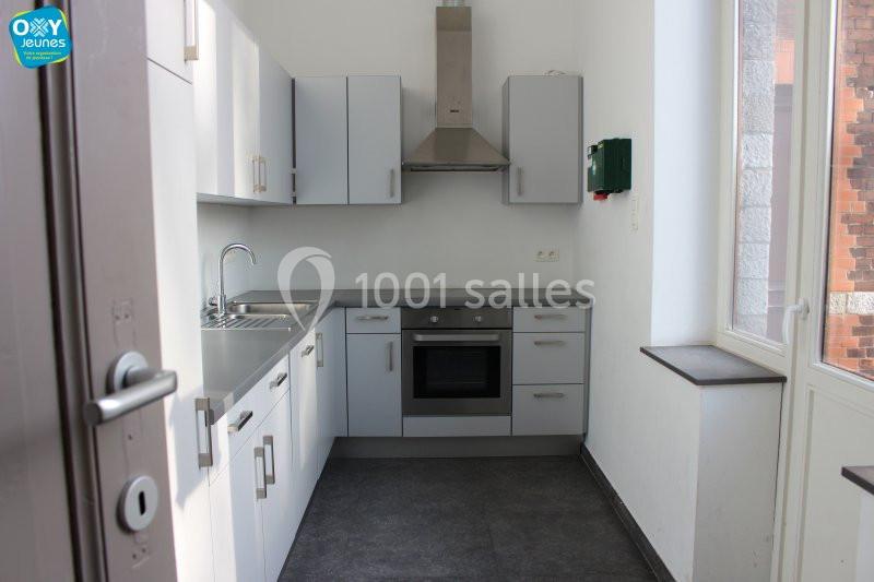 Cuisine moderne avec meubles blancs, évier en inox, plaque de cuisson, hotte et fenêtre laissant entrer la lumière.