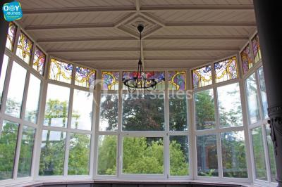 Grande maison en briques rouges avec deux tours, entourée de pelouse et de voitures garées devant.