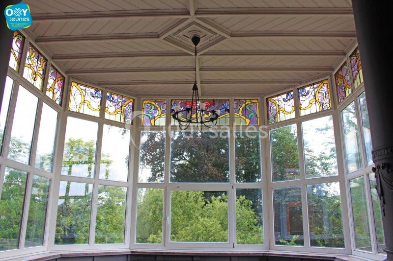 Baie vitrée avec vitraux colorés en partie haute, offrant une vue sur des arbres et un ciel dégagé.