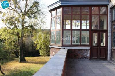 Grande maison en briques rouges avec deux tours, entourée de pelouse et de voitures garées devant.