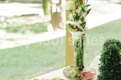 Une mariée en robe blanche est assise sur un banc en bois décoré des lettres ’A&J’, tenant un bouquet de fleurs.