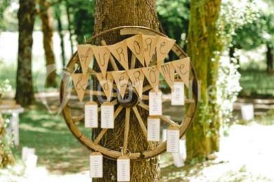 Une mariée en robe blanche est assise sur un banc en bois décoré des lettres ’A&J’, tenant un bouquet de fleurs.