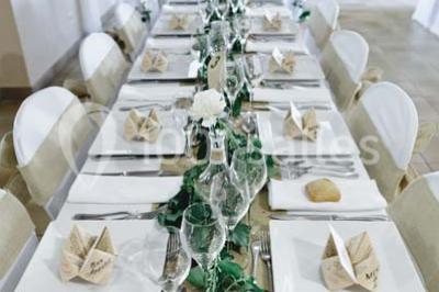 Une mariée en robe blanche est assise sur un banc en bois décoré des lettres ’A&J’, tenant un bouquet de fleurs.