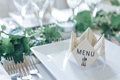 Une mariée en robe blanche est assise sur un banc en bois décoré des lettres ’A&J’, tenant un bouquet de fleurs.